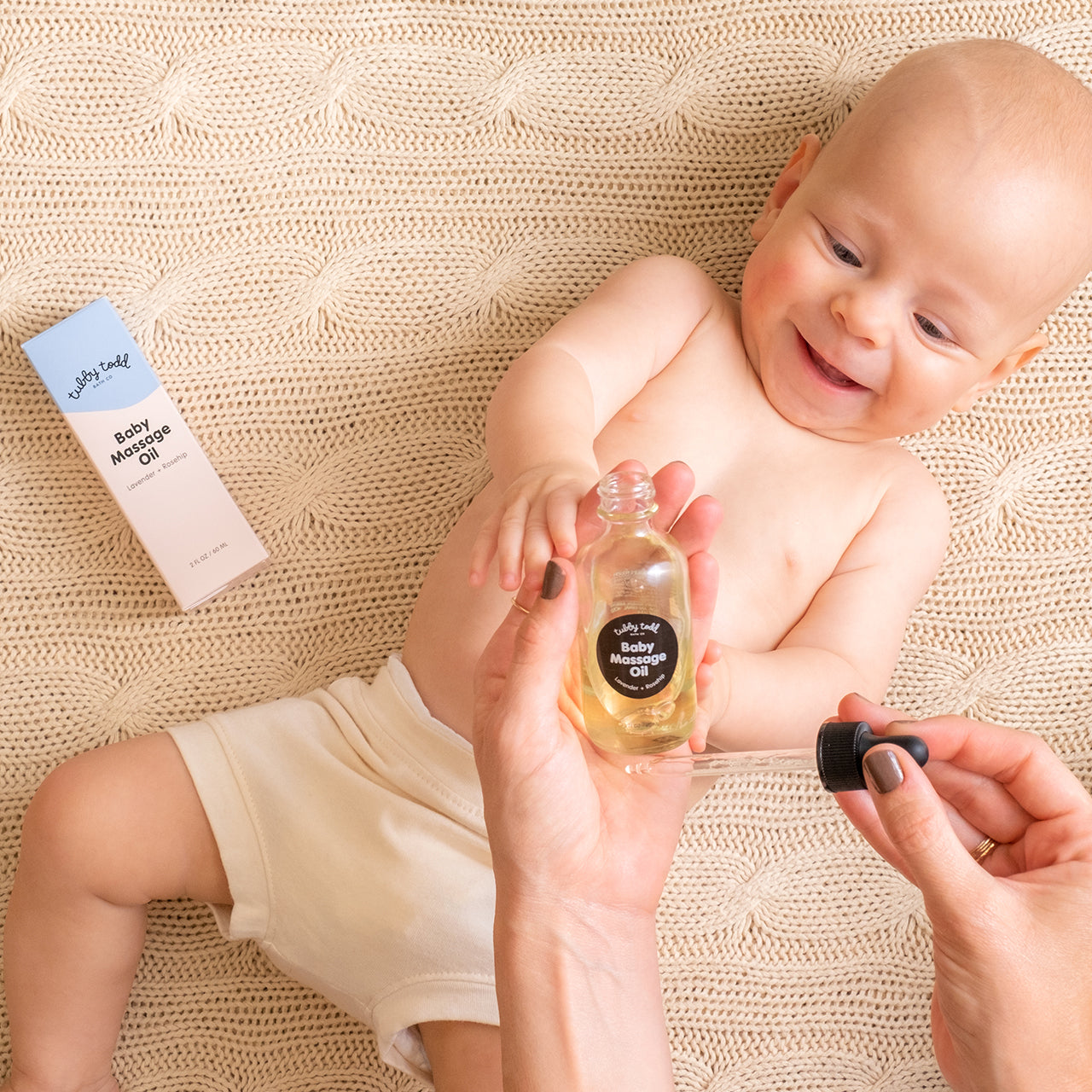 Mom is dropping baby massage oil on her hand and baby lying on the bed.